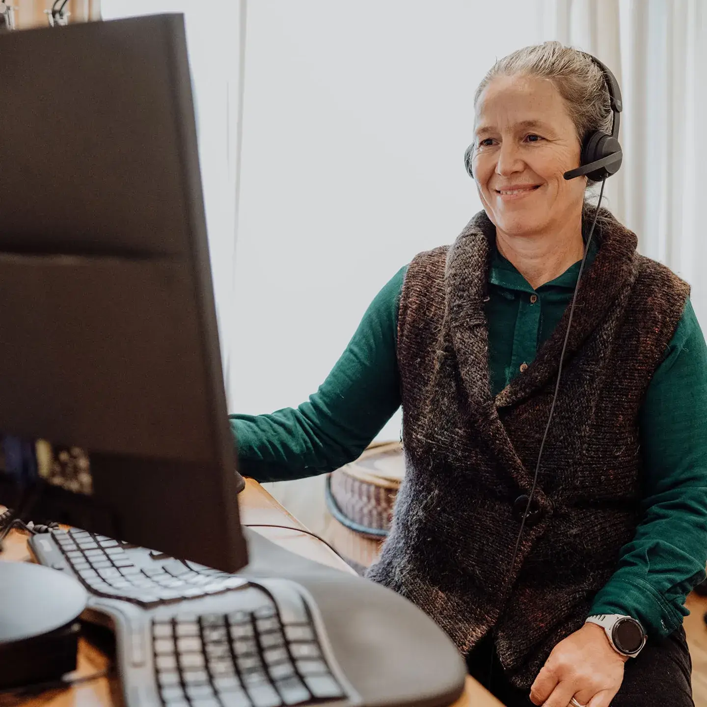 Dawn sits on a chair with a headset on looking at a computer conducting a telehealth consultation
